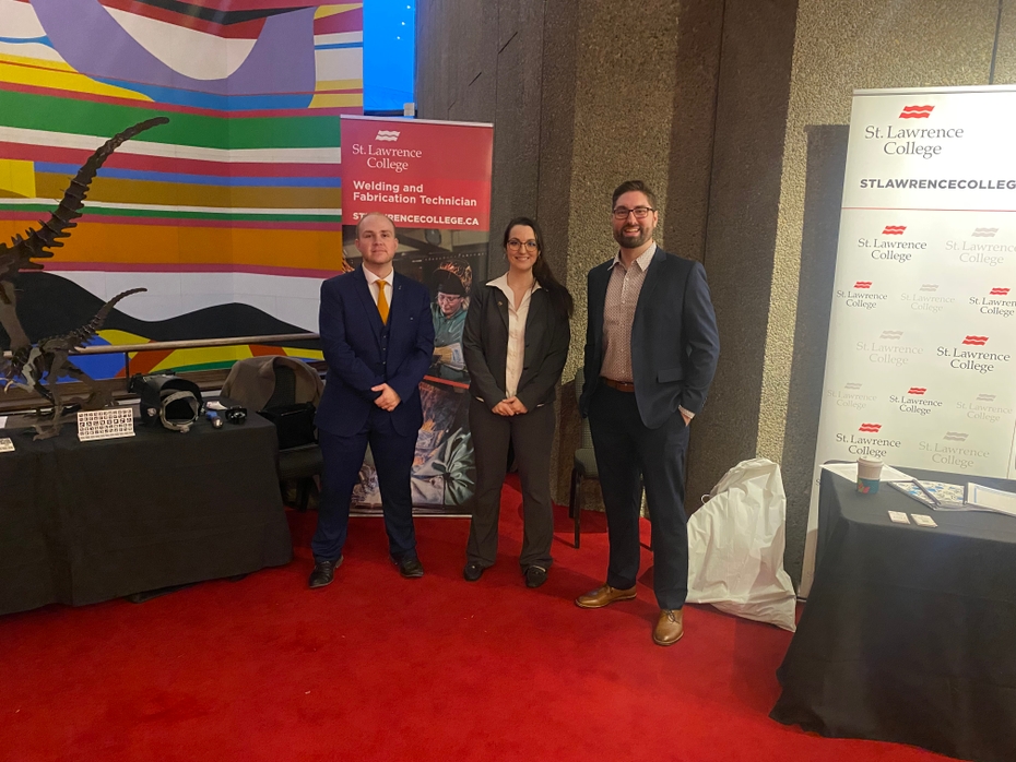 Jadon Hook, Ariane Morin, and Steve Janssens stand in front of the SLC display tables at CICan on the HIll